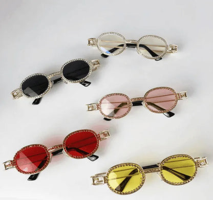 Five pairs of small vintage oval sunglasses with gem-embellished golden frames in black, clear, pink, red, and yellow lenses