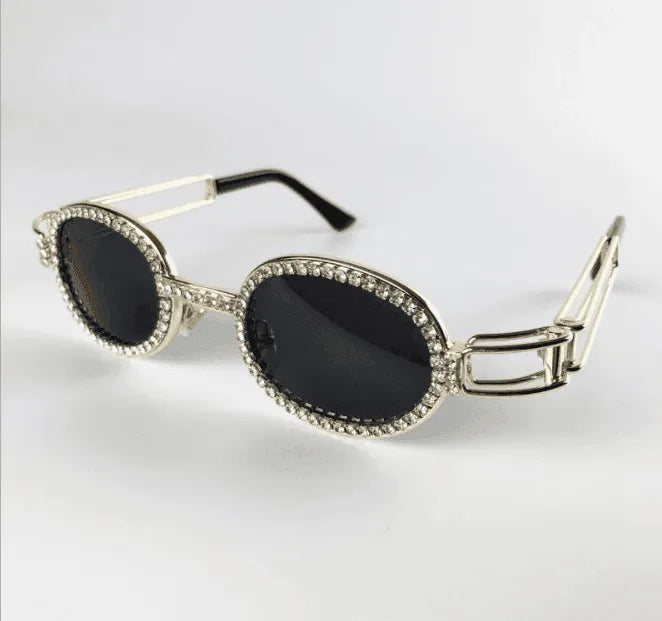 Oval black lens sunglasses with silver frame encrusted with clear rhinestones on white background