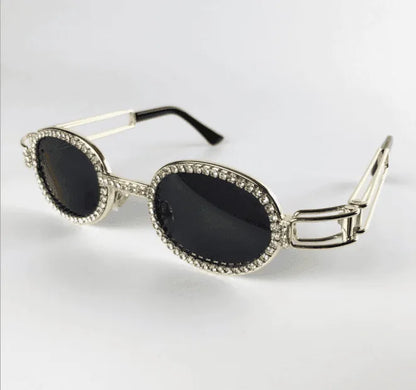 Oval black lens sunglasses with silver frame encrusted with clear rhinestones on white background
